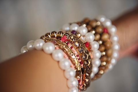 a woman's arm with several stacked red, white, and gold beaded bracelets