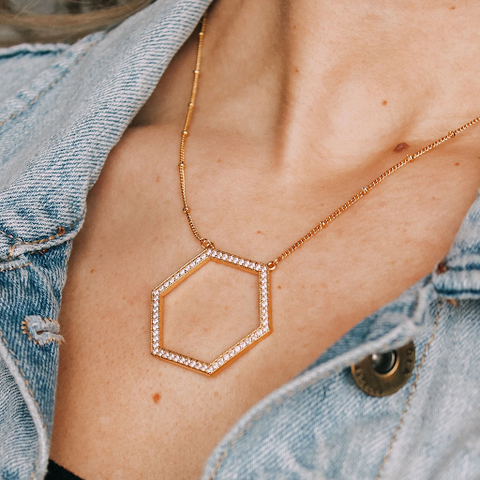 A woman wearing a necklace with a large gold hexagon. 