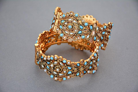 two gold bangles filled with blue stones on a gray table