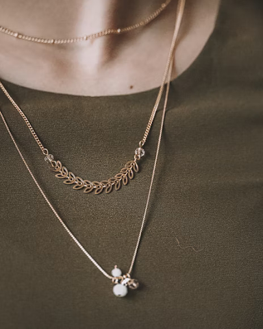 A charm necklace is worn with two other necklaces of varying lengths. 