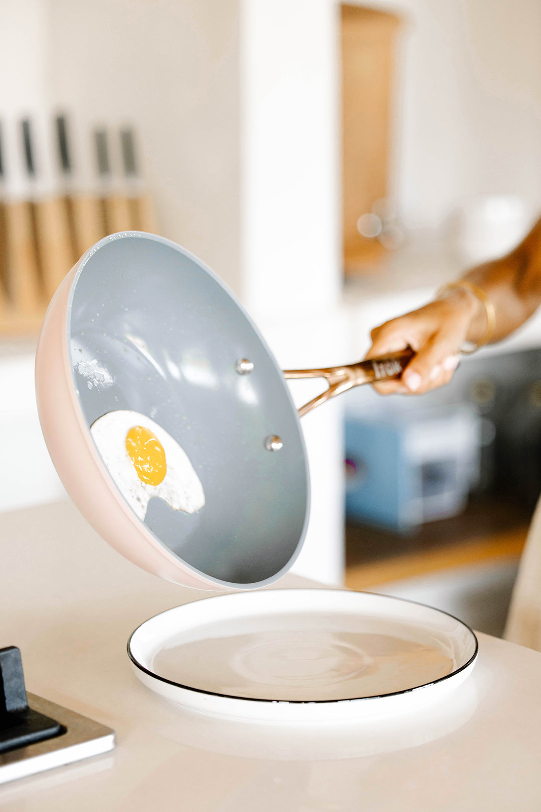 A person sliding a fried egg from a pan onto a white plate.