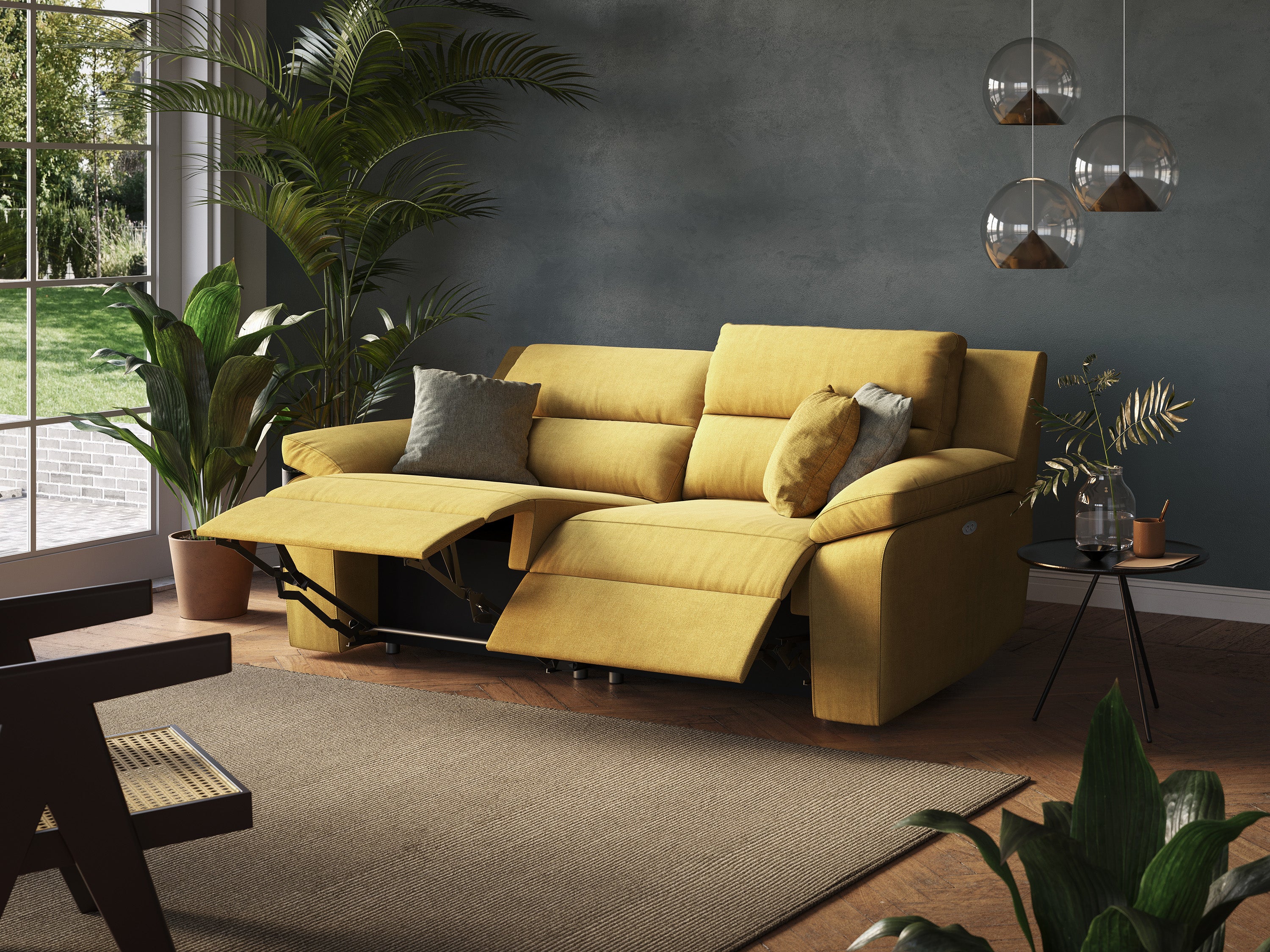 Un elegante soggiorno presenta un Romeo Divano relax con recliner elettrico in morbido tessuto impermeabile T02 in giallo di Divani.Store, completo di poggiapiedi esteso e completato da cuscini grigio chiaro e giallo senape. Le pareti verdi ospitano lampade a sospensione in vetro e piante rigogliose incorniciano lo spazio. Una grande finestra offre luce naturale, illuminando il pavimento in legno e il tappeto neutro.