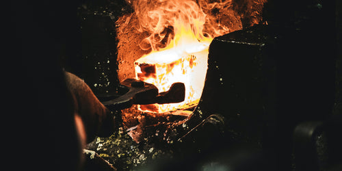 Heavy metal tongs pulling a block of molten steel out of a forge.