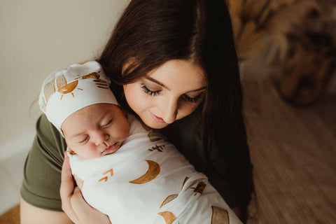 An adorable baby wrapped in an organic cotton swaddle in snuggly jacks arizona print being held by its mother is a sweet embrace.