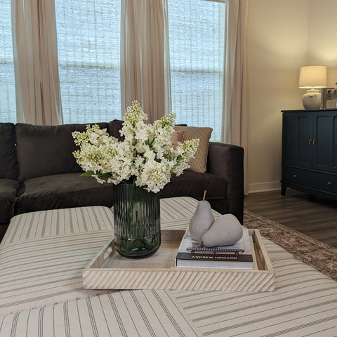 Faux lilacs in a smokey gray fluted vase, in a living room. 