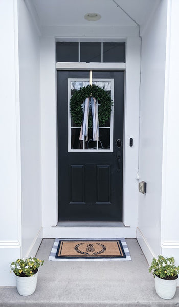 Front entry picture of small porch with layered gingham and pineapple rugs and potted flowers.