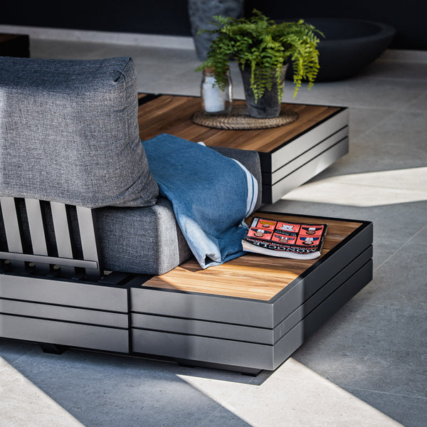 Contemporary aluminium sofa set with teak side table layered with blue throw & coffee table book