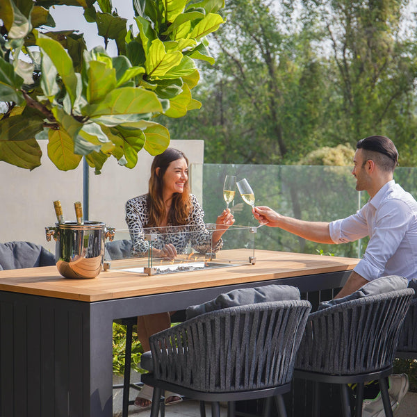 Couple clinking glasses around the monterrey 6 seat grey bar set with teak table top