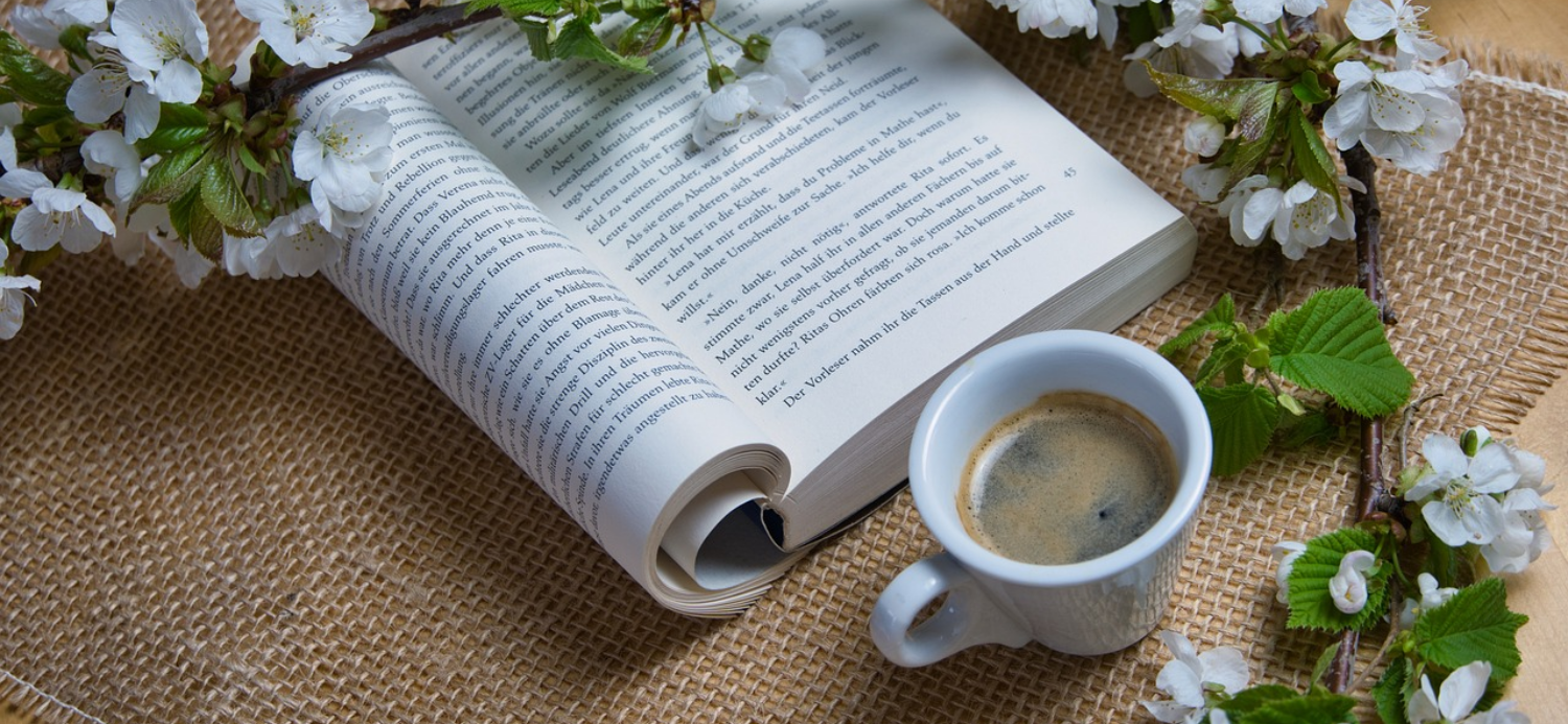 Black coffee on a table with open book and white flowers