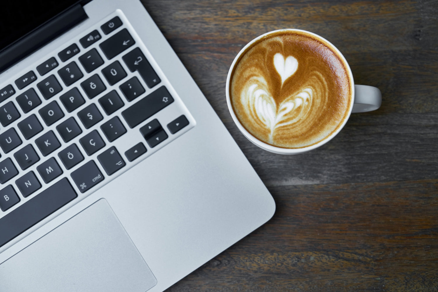 Latte art on home coffee sat beside a MacBook