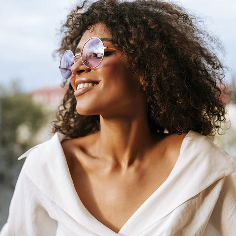 Smiling woman wearing sunglasses and white top.