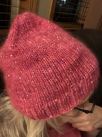 A woman wearing a pink hat hand knit with paillettes, mohair and wool.