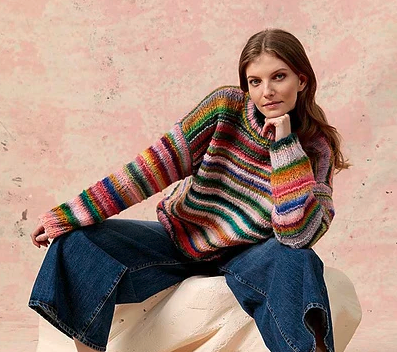 A young woman sitting with her left hand supporting her chin and the right hand resting on her knee. She is wearing sweater PTO-031_02 knit with Lang Yarns Cloud