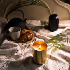 Gold scented candle pictured with coffee and a croissant