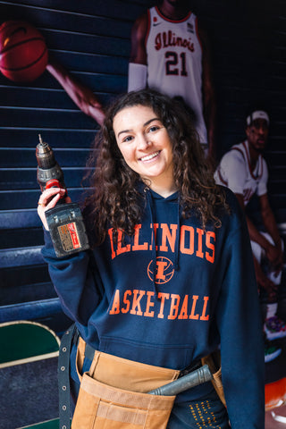 woman in illinois basketball hoodie holding a drill while building out an illinois basketball store in chicago