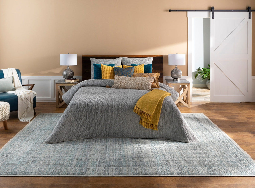 A bedroom with a cozy rug extending around the edges of the bed, placed on a beautiful hardwood floor.