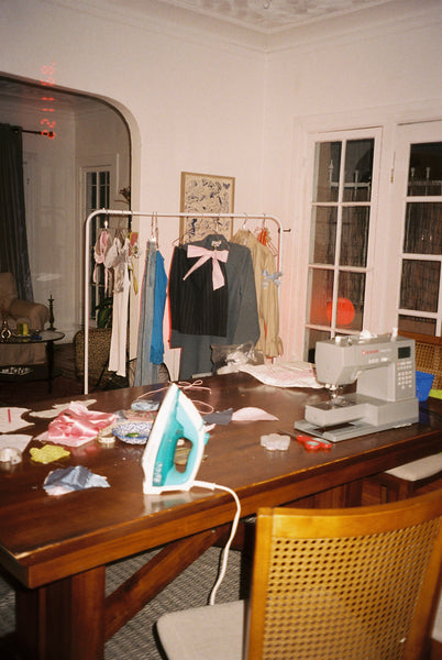 A messy room with an iron, sewing machine and handmade garments scattered