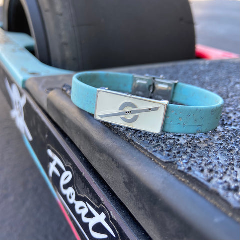 Stoke Saver bead with white background on a full turquoise color cork cordage strap, bracelet is resting atop the foot pad of a Onewheel XR with The Float Life sticker in the foreground
