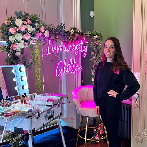 Luminosity Glitter's Lauren stood next to the luxury eco glitter bar set up, backdrop with eucalyptus garlands and a hot pink neon sign
