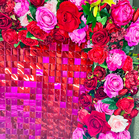 Hot pink and red mosaic sequin wall hire surrounded by a floral garland filled with pink and red flowers