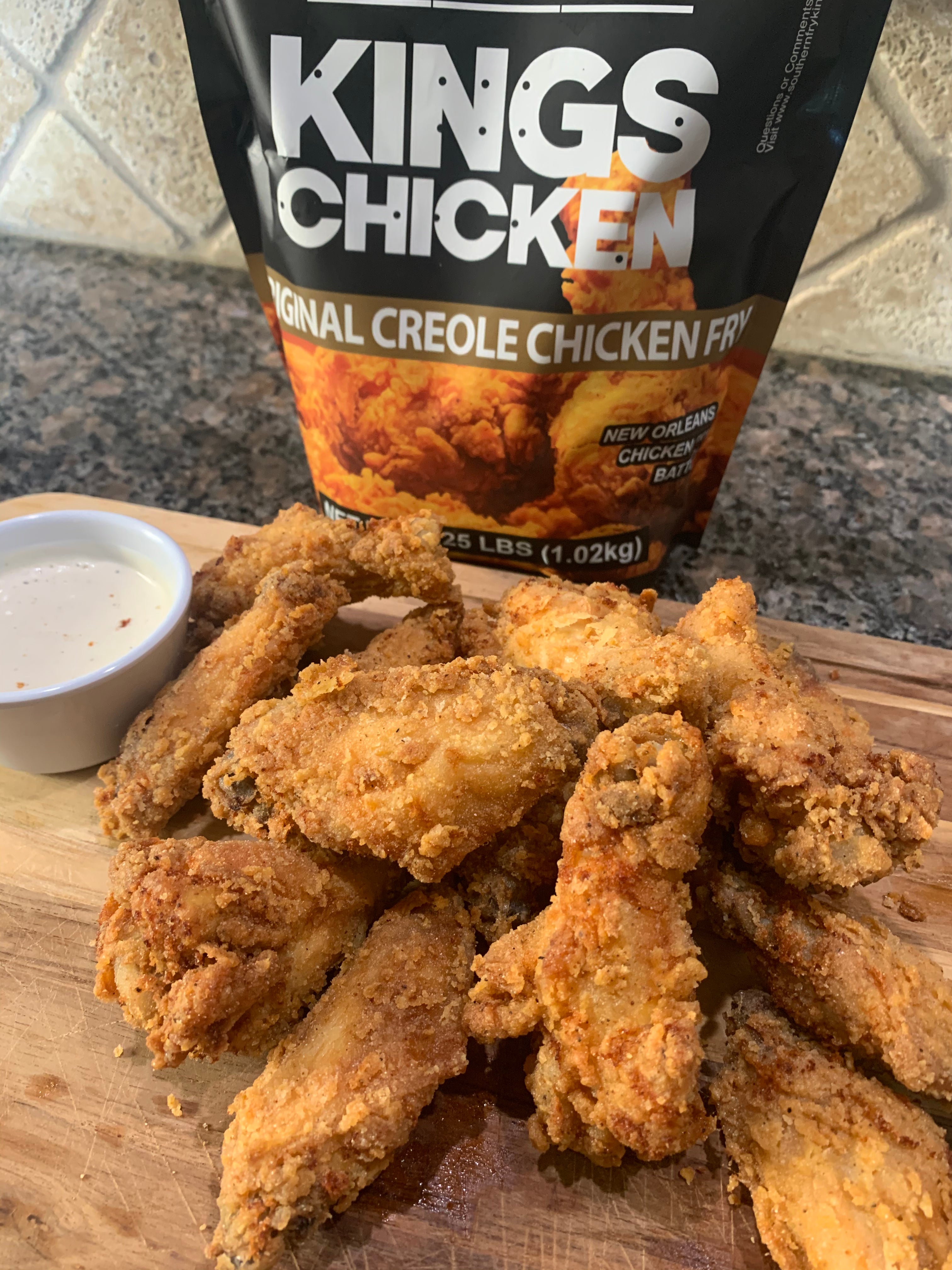 Fried chicken wings with dipping sauce and a bag of King's Chicken Creole Chicken Fry.