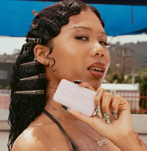 Woman with wet hair clips holding a bar of soap for skin flare ups outdoors with bold nail art