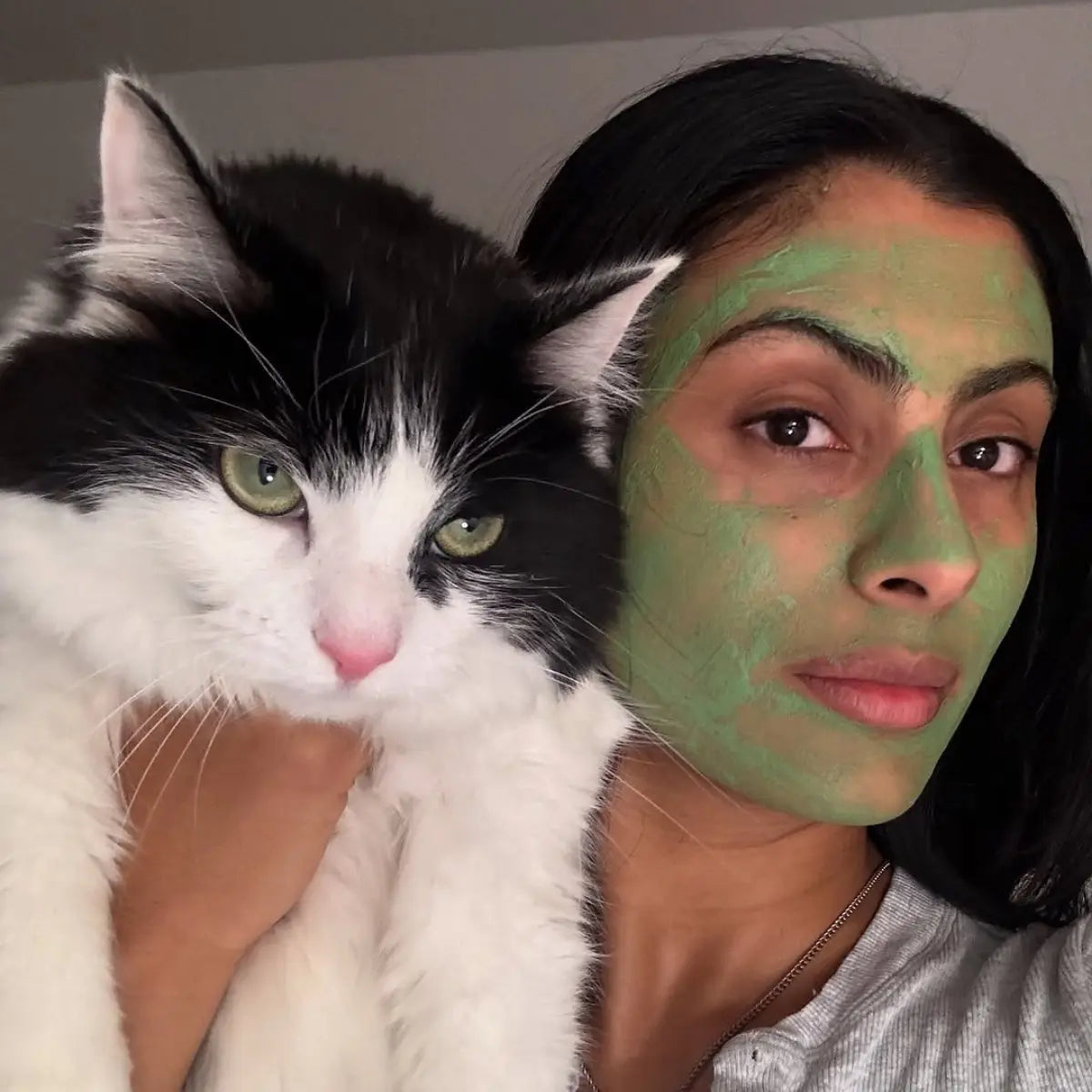 Acne skincare green face mask applied on woman posing with fluffy black and white cat.