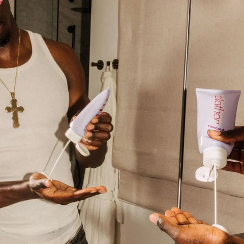 Brightening serum being dispensed from a Topicals Slather tube by a man in front of a bathroom mirror.