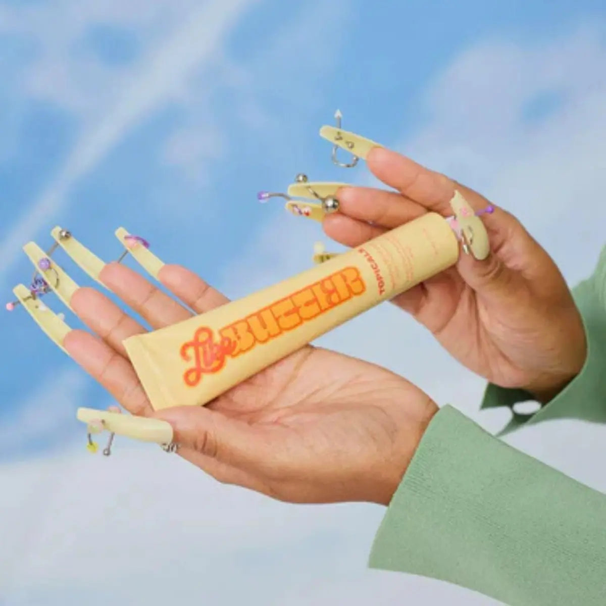 Ceramides for skin displayed in a model’s hand with decorative nails and a blue sky background.