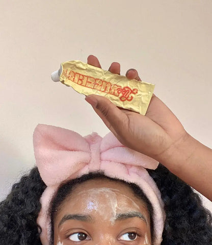 Woman holding a tube of cream for dark spots with visible facial product applied