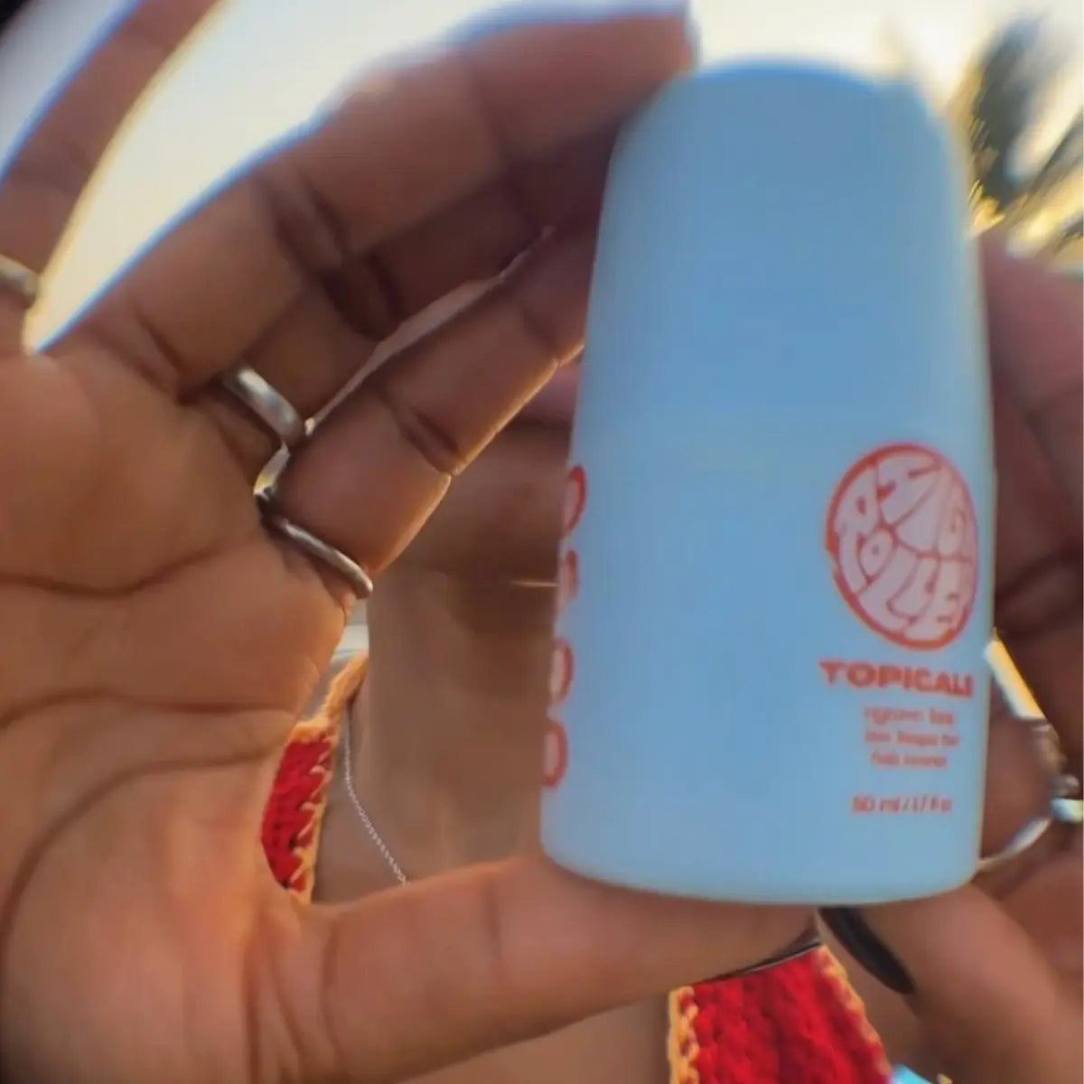 Acne skincare High Roller product held in focus by person with rings against outdoor light.