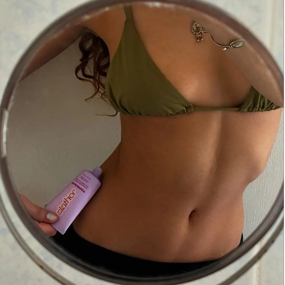 Skin lightening serum displayed by a woman in a mirror reflection, applying the product to her toned stomach