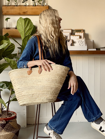 a lady sitting on a stool holding a large woven bag