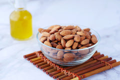 Glass bowl full of almonds with a glass of oil behind it