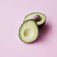 Ripe avocado cut in half showing inside flesh against a pink background