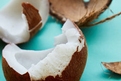 opened coconut showing white flesh against an aqua colored background