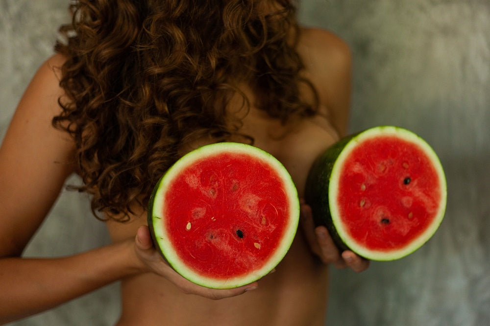 young naked woman hiding behind two halves of watermelon