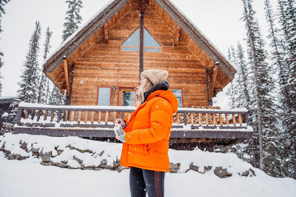 jeune femme portant un manteau orange devant un chalet