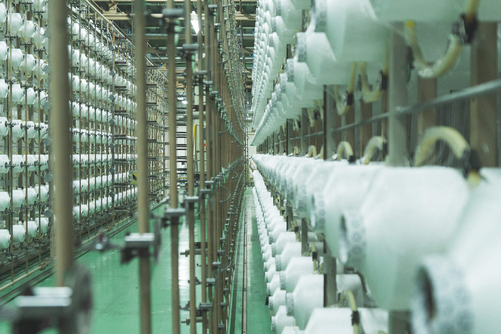 データで管理され、ほとんど人がいない工場で何千もの糸が整列され、織り機まで伸びる