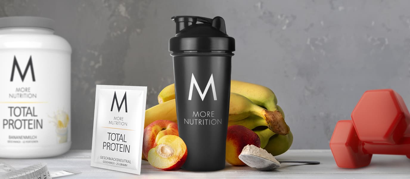 Zu sehen ist ein Shaker mit einem Proteinshake neben Obst, Proteinpulver und Sportutensilien.