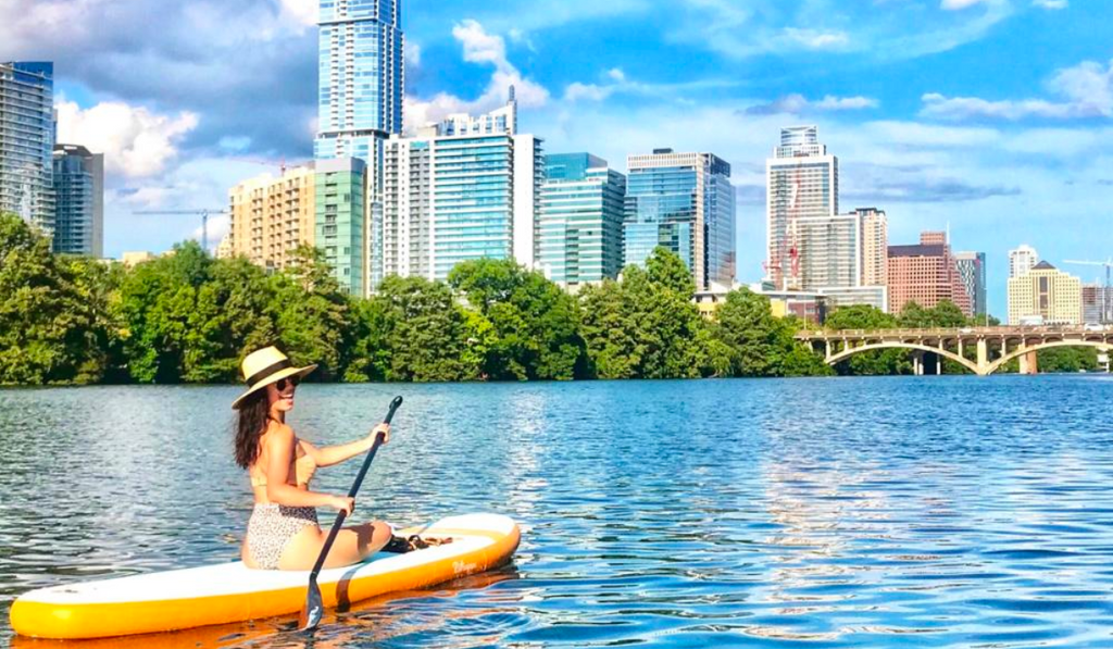 Woman paddle boarding on Lake Austin with yellow paddle board and the city of Austin Texas in background