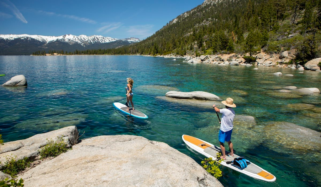Two paddle boarders on Lake Tahoe with clear water and rocks.