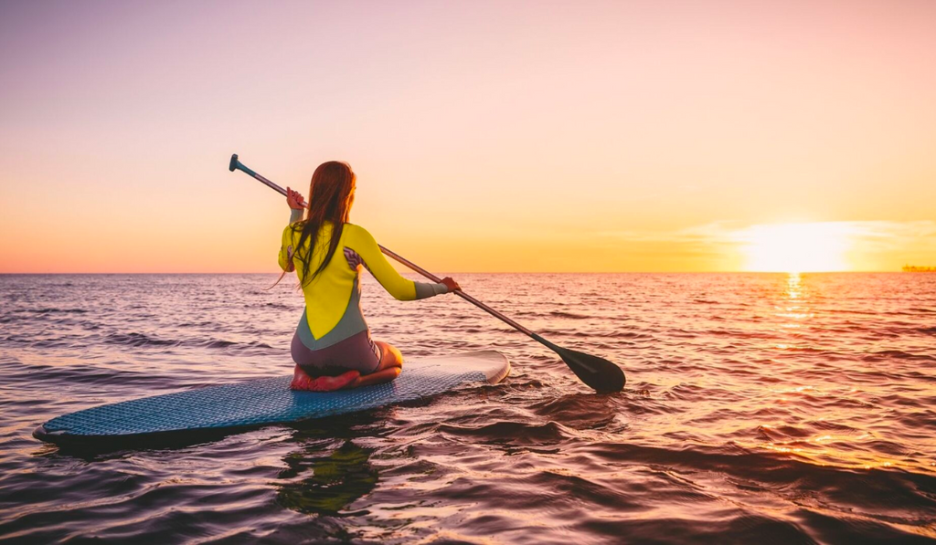 Woman paddle boarding on the Florida waters with yellow sunset