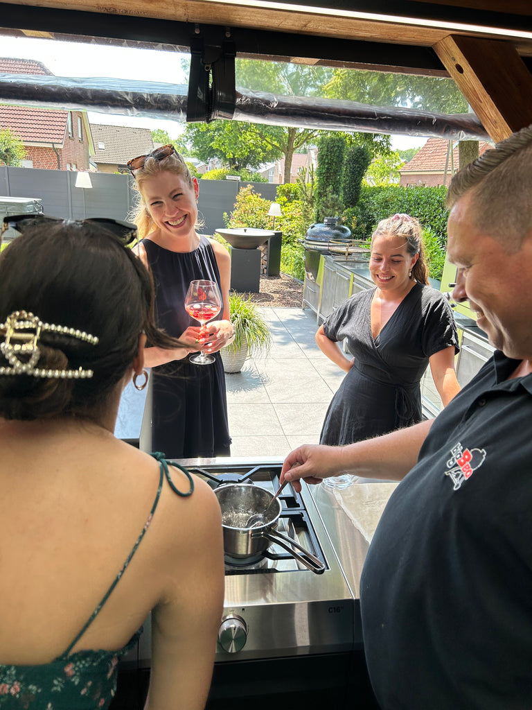 Ein Mann kocht in seiner Outdoor-Küche und unterhält sich mit drei Frauen