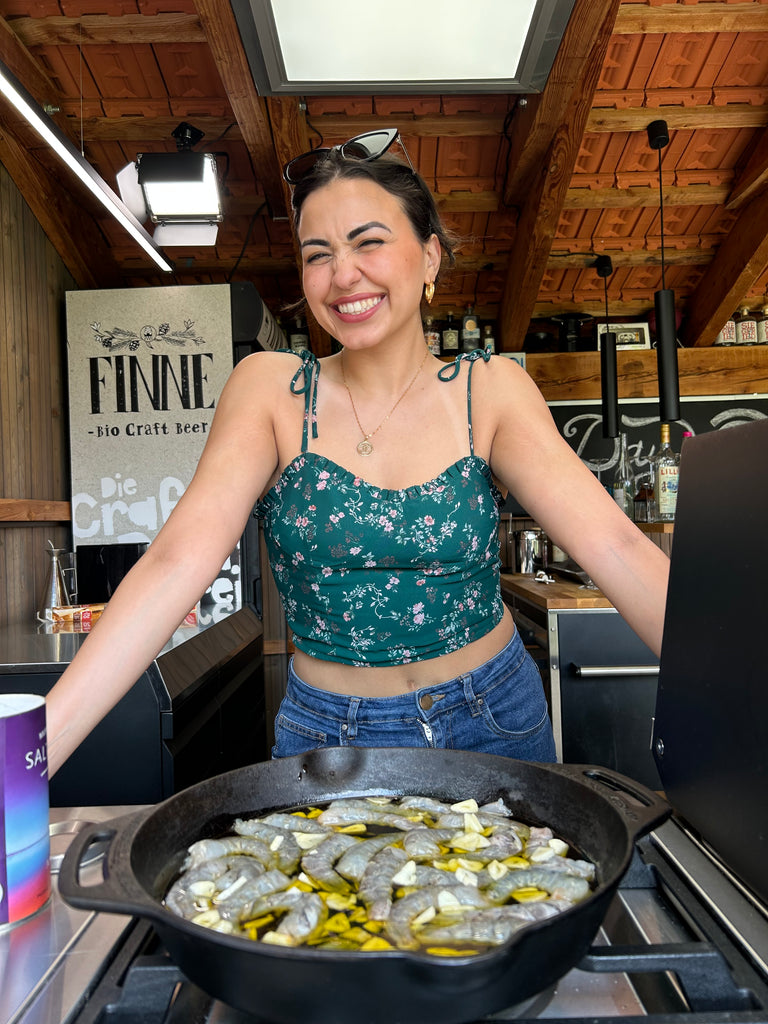 Eine Frau steht an einer Outdoor-Küche mit einer Gusseisenpfanne voller Gambas