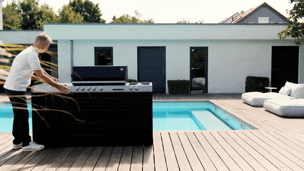 Ein Mann verschiebt Module einer Outdoor-Küche vor einem Swimming Pool