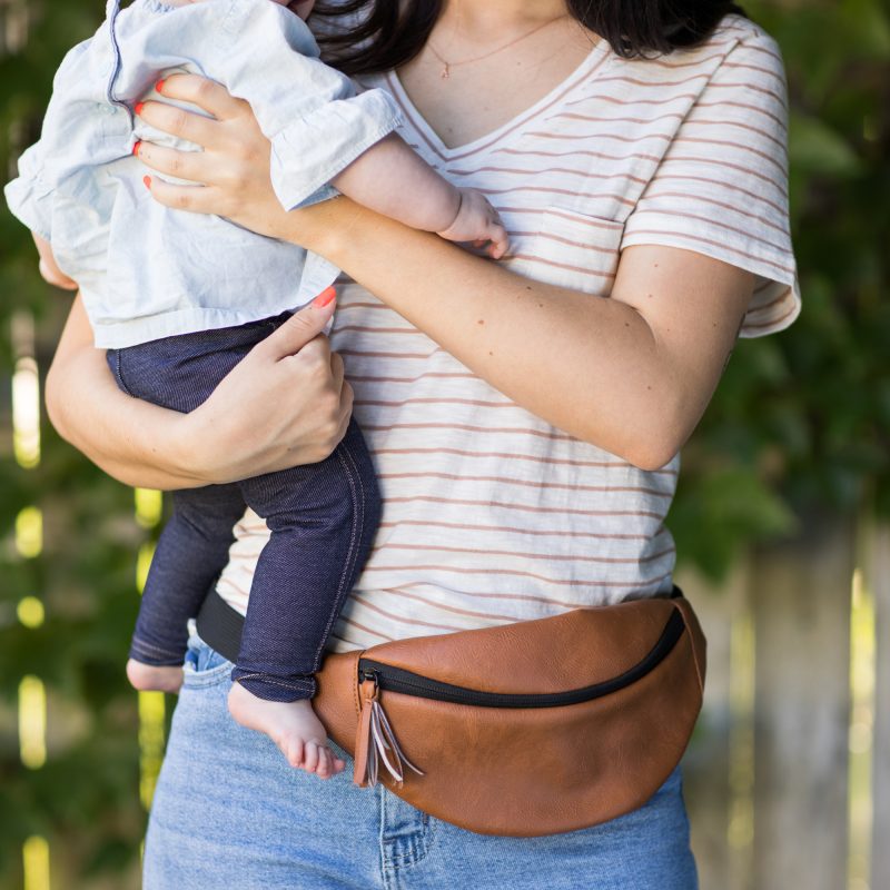 Woman holding baby and wearing hip pack from the Stroller Organizer with Hip Pack