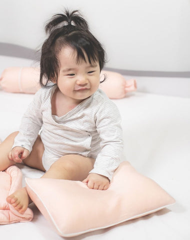 baby smiling holding ava and ava organic bamboo lyocell baby pillows in pink blush