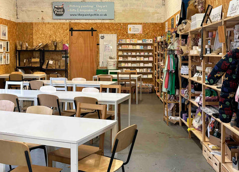 A view of the cafe including white tables and brown and white chairs and homeware and gifts along the edge of the room