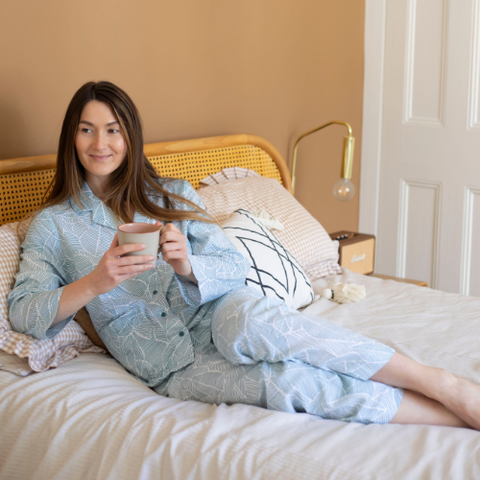 A woman drinking tea in light blue pyjamas in bed